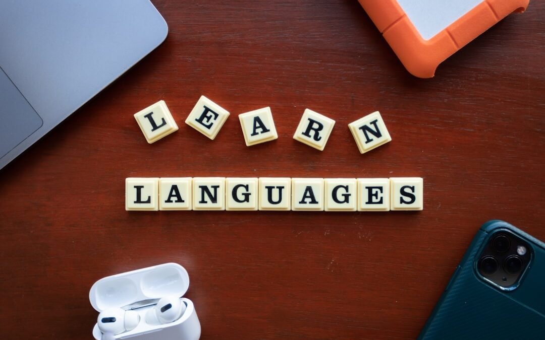 Learn Languages spelled out in letter tiles with modern study tools including phone, earbuds and notebooks on wooden desk - Photo by Unsplash