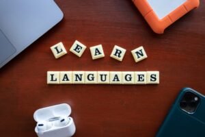 Learn Languages spelled out in letter tiles with modern study tools including phone, earbuds and notebooks on wooden desk - Photo by Unsplash