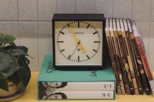 Minimalist desk clock sitting on a stack of books, representing focused and timed language learning sessions. Photo by Gemma Evans on Unsplash