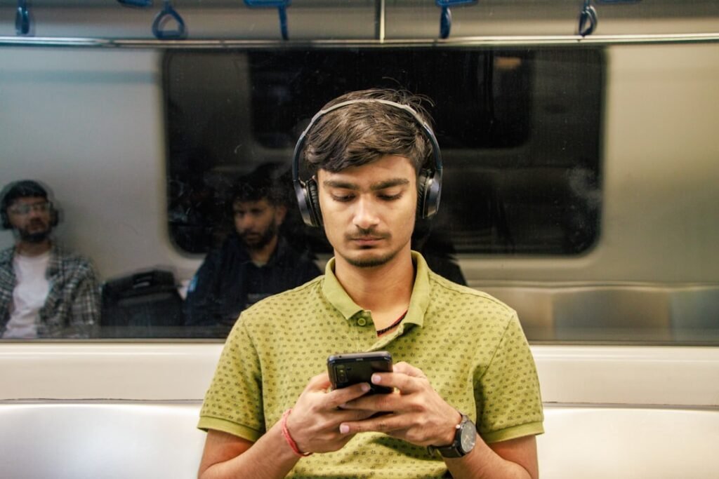 Young man using headphones and smartphone on public transit, demonstrating immersion stacking by learning during commute time